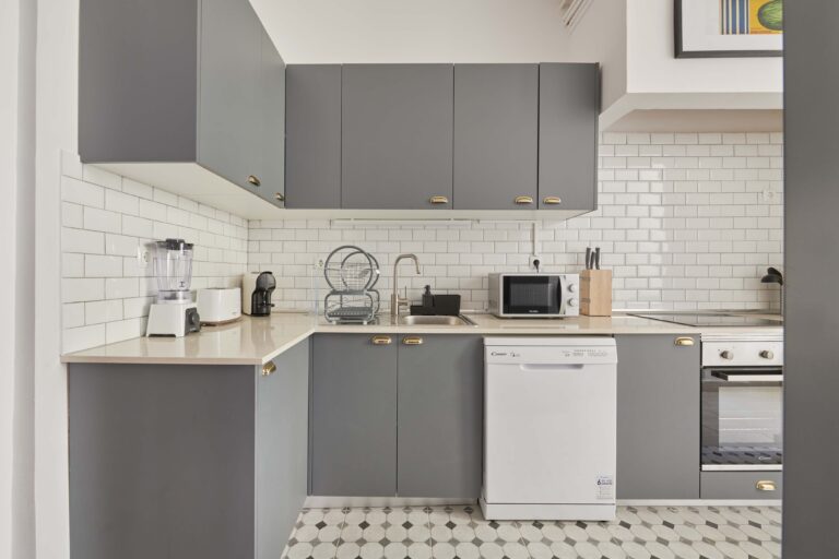 Modern kitchen with grey cabinets, white backsplash, appliances, and patterned tile floor.