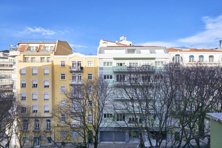Urban buildings with yellow and green facades, balconies, trees, under a clear blue sky.