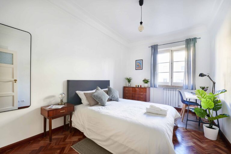 Bright bedroom with bed, wooden furniture, large mirror, and potted plants near window.