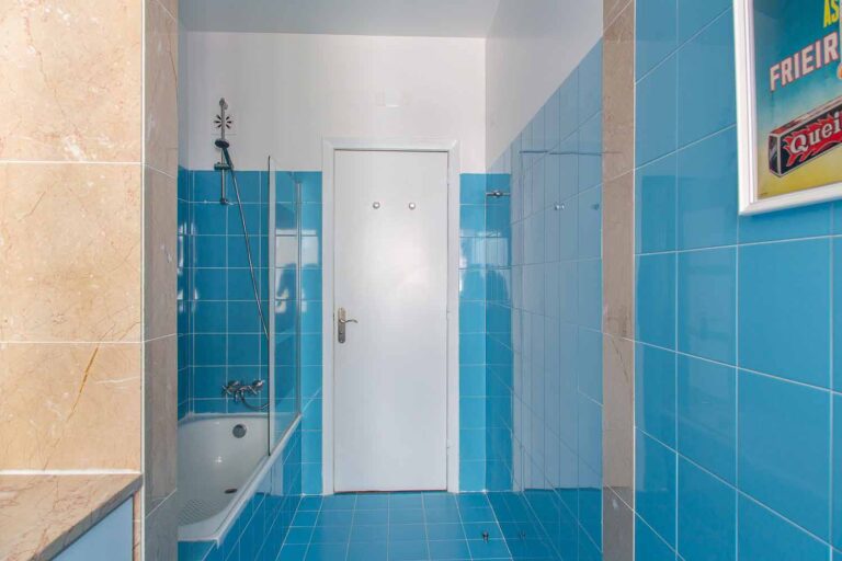 Bathroom with blue tiles, white door, and bathtub with showerhead; poster on right wall.