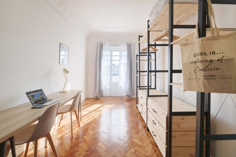 Bright room with wooden table, laptop, chairs, lamp, shelves, tote bag, and natural light.