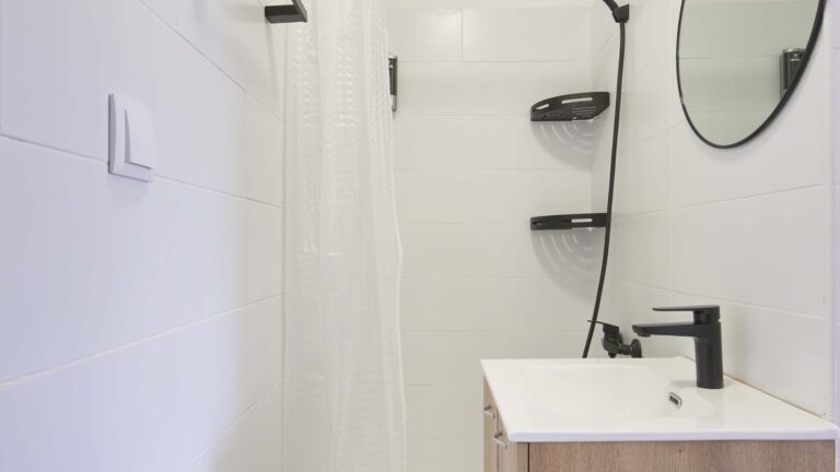 Minimalist bathroom with white tiles, circular mirror, black fixtures, and simple shower curtain.