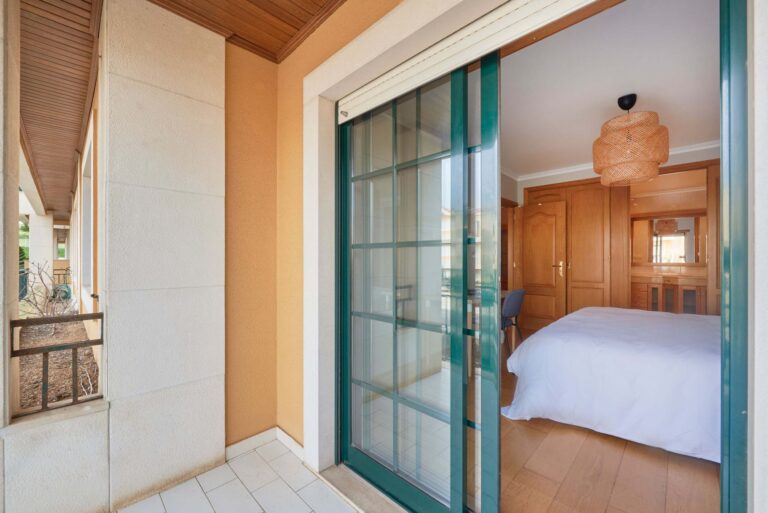 Bedroom with sliding glass door to patio, wooden furniture, white bed, and woven light fixture.