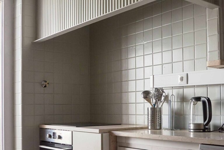 Modern kitchen corner with stovetop, utensils, kettle, and tiled backsplash.